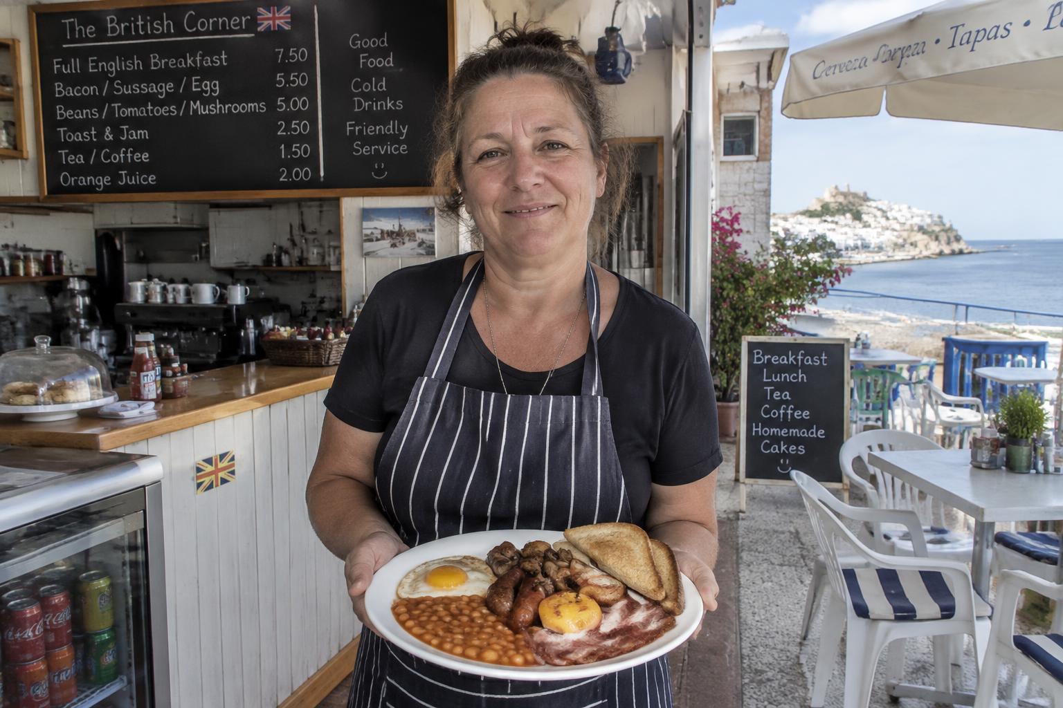 Owner of a British-run breakfast café holding a full English breakfast